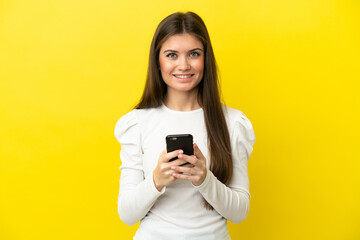 Young caucasian woman isolated on yellow background sending a message with the mobile