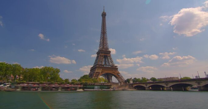 The Eiffel tower timelapse near river Seine in Paris. Ship and boats on river at sunny summer day. The Eiffel Tower is called the most visited paid and most photographed attraction in the world