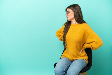 Young caucasian woman sitting on a chair isolated on blue background suffering from backache for...