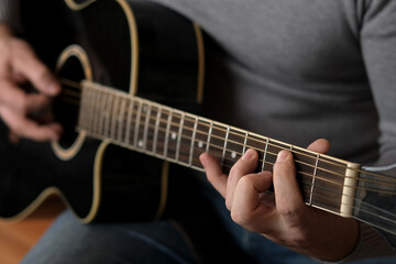 Obraz na płótnie Canvas Playing the guitar. Strumming black acoustic guitar. Musician plays music. Man fingers holding mediator. Male hand playing guitar neck in dark room. Unrecognizable person rehearsing, fretboard closeup