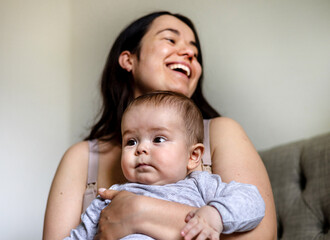mother and baby son boy hugging kissing caresses cuddling sitting on sofa talking at...