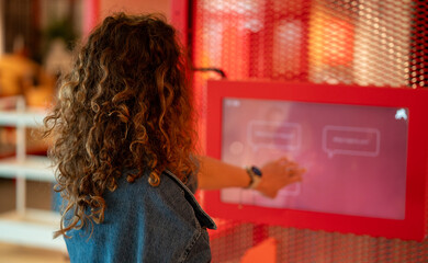 Curly hair woman using touch screen and buy tickets. Taking interactive quiz in modern art museum.