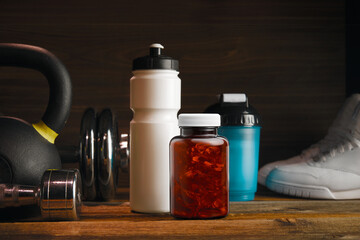 Close-up shot of sealed, unlabeled, clear jar of gel pills, shaker and fitness white water bottle with sport equipment on background. Sport and Fitness Mock-up concept.