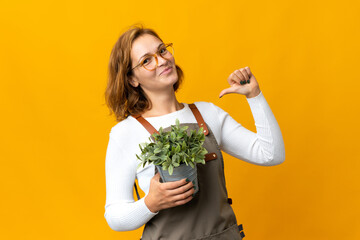 Young Georgian woman holding a plant isolated on yellow background proud and self-satisfied