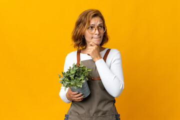 Young Georgian woman holding a plant isolated on yellow background having doubts and thinking