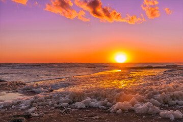 Obraz premium Sun setting on the horizon over the sea and the beach covered with golden foam.