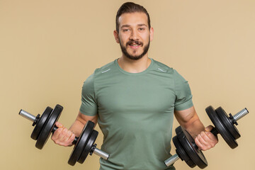 Fototapeta na wymiar Athlete young sportive man working out. Middle eastern bodybuilder instructor sportsman guy training biceps, weightlifting dumbbells indoors on studio beige background. Strong, exercise, motivation