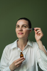 A nice woman with clean skin should apply oil, essence from a pipette to her face.