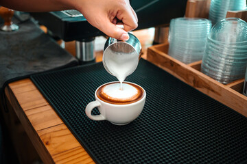 Barista hand pouring milk into coffee making a cappuccino. Professional barista preparing coffee on the counter.