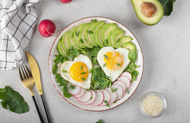 Healthy romantic breakfast - heart-shaped fried eggs served with avocado and radish, Top view