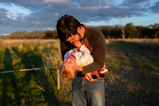 Father and toddler child playing together in rural farm paddock setting laughing and swinging