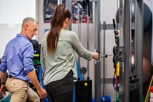Woman working with physio at physiotherapist clinic using equipment to recover from injury