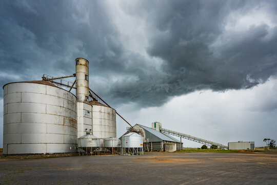 Rain falling from a dramatic stormfront over grey grain storage silos in a rural setting