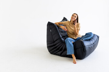 Young woman talking on phone in bag armchair against white background