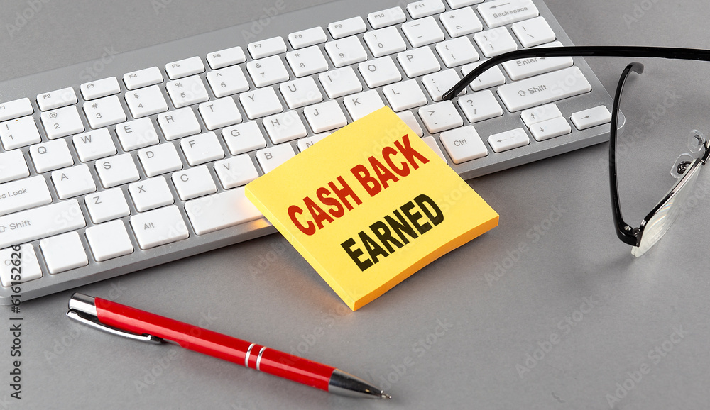 Poster cash back earned text on a sticky with keyboard, pen glasses on grey background
