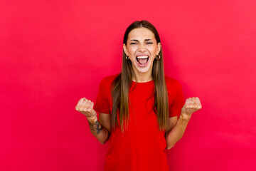 Achievement concept. Young woman in casual shirt raised fists, eyes close up isolated on red...