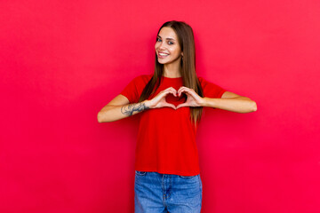 Portrait of happy smiling girl in casual isolated over red background. Heart sign with hands.