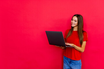Pretty young woman in casual holding laptop in the office, isolated over red background.