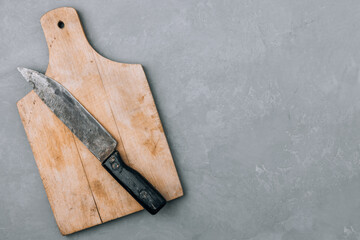 Wooden chopping cutting board and old vintage kitchen knife on gray stone background, top view,