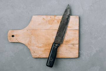 Wooden chopping cutting board and old vintage kitchen knife on gray stone background, top view,