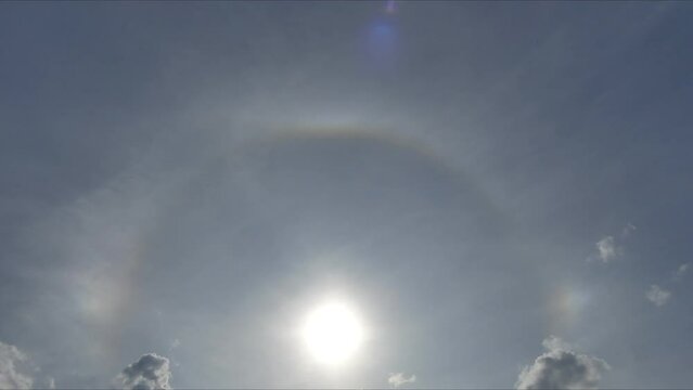 Blue sky with Halo around the sun and moving clouds - time lapse. Optical phenomenon - upper tangent arc and sub parhelia on the clouds cirrostratus in the upper troposphere.