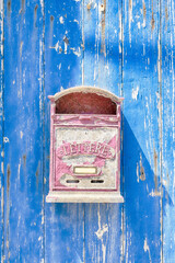 Pink vintage metal mailbox on a bright blue wall in Italy.