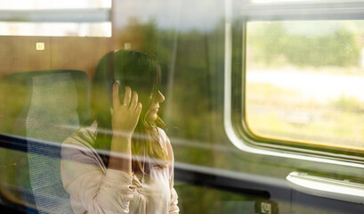 A woman on the train wearing headphones and looking out the window