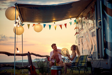 Young couple talking and laughing. Sunset in front of camper rv. Travel, fun, love, togetherness, lifestyle concept. - Powered by Adobe