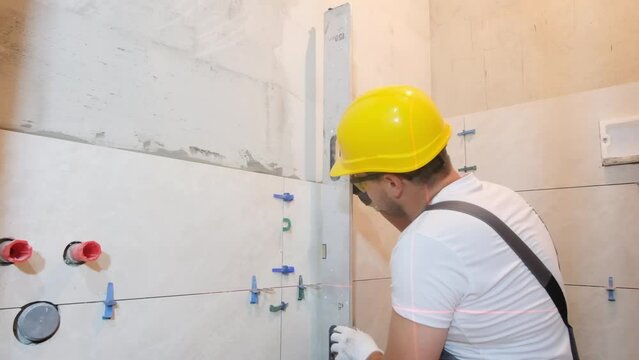 The builder measures the vertical deviation of the wall during the installation of ceramic tiles. 