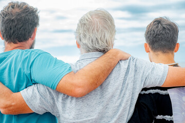 Rear view of family multi generation, father, teenage son and grandfather hugging with love....