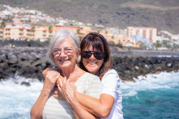 Fototapeta na wymiar Portrait of Happy Couple of Mature Women Hugging with Feeling in Vacation at Sea Under the Sun. Elderly females Enjoying Freedom and Relax
