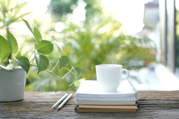 white coffee cup and books and pencils and pothos plant pot on brown wooden table