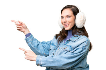 Young caucasian woman wearing winter muffs over isolated background pointing finger to the side and...