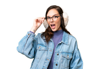 Young caucasian woman wearing winter muffs over isolated background with glasses and surprised