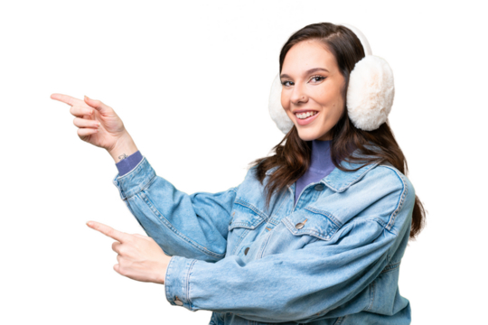 Young caucasian woman wearing winter muffs over isolated background pointing finger to the side and presenting a product