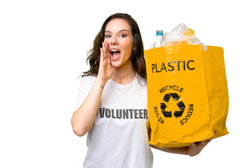 Young caucasian woman holding a bag full of plastic bottles to recycle over isolated background...