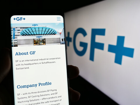 Stuttgart, Germany - 06-18-2023: Person holding cellphone with webpage of Swiss company Georg Fischer AG (GF) on screen in front of logo. Focus on center of phone display.