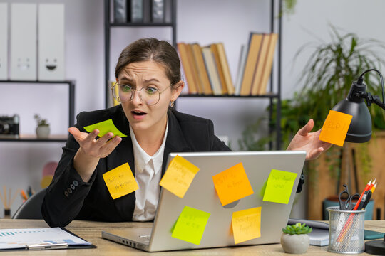 Tired exhausted young business woman working on laptop at office with many sticker task inscriptions. Freelancer girl busy occupation feels sad boredom overworked multitasking. Panic attack, deadline