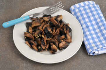 Champignons cuisinés avec de l'ail dans une assiette avec une fourchette en gros plan sur fond gris