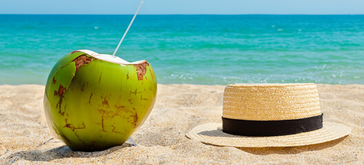 Hat and a Coconut Water on the beach. Closeup on the sand in the foreground with blurred sea in the background.
