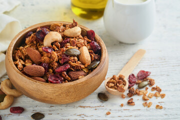 Homemade granola in glass jar with greek yogurt or milk and cashews, almonds, pumpkin with dried cranberry seeds in on white rustic wooden table background. Healthy energy breakfast or snack. Top view