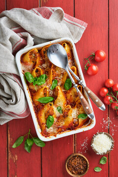Cannelloni or conchiglioni. Baked stuffed pasta shells with bolognese meat sauce, tomatoes, basil on rustic red wooden table. Traditional Italian bolognese baked pasta with parmesan. Italian cuisine.