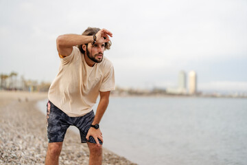 Beautiful young man running on the sandy sea beach in summer wearing a sports clothing, working out outdoors - Powered by Adobe