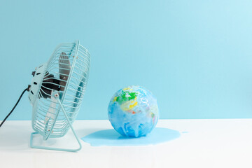 Global warming concept with a little blue fan cooling the world globe melting on white and blue...