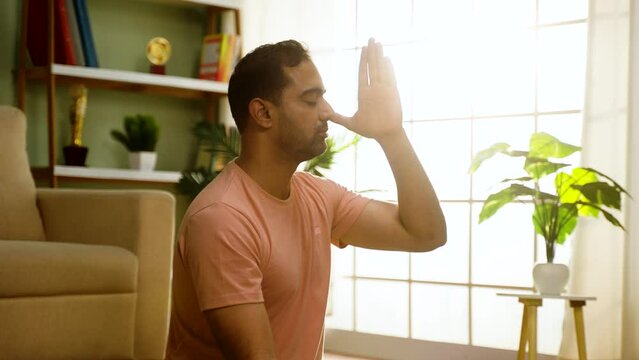 handheld shot of Indian man doing nostril breathing pranayama yoga by closing eyes at home - concept of mindfulness, healthy lifestyle and morning rituals