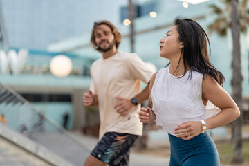 Cheerful young multi-ethnic urban couple running alongside the beach wearing casual summer sport clothing. Jogging in the city