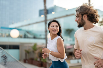 Cheerful young multi-ethnic urban couple running alongside the beach wearing casual summer sport clothing. Jogging in the city