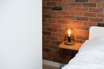 Reading lamp near the bed in the bedroom. Interior design in modern loft apartment. Cozy bedroom with home decor, bedside nightstand with shining lamp near white wall with copy space for text