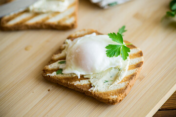 Fried toast bread with spread and poached egg, on a wooden table.