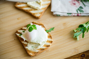 Fried toast bread with spread and poached egg, on a wooden table.